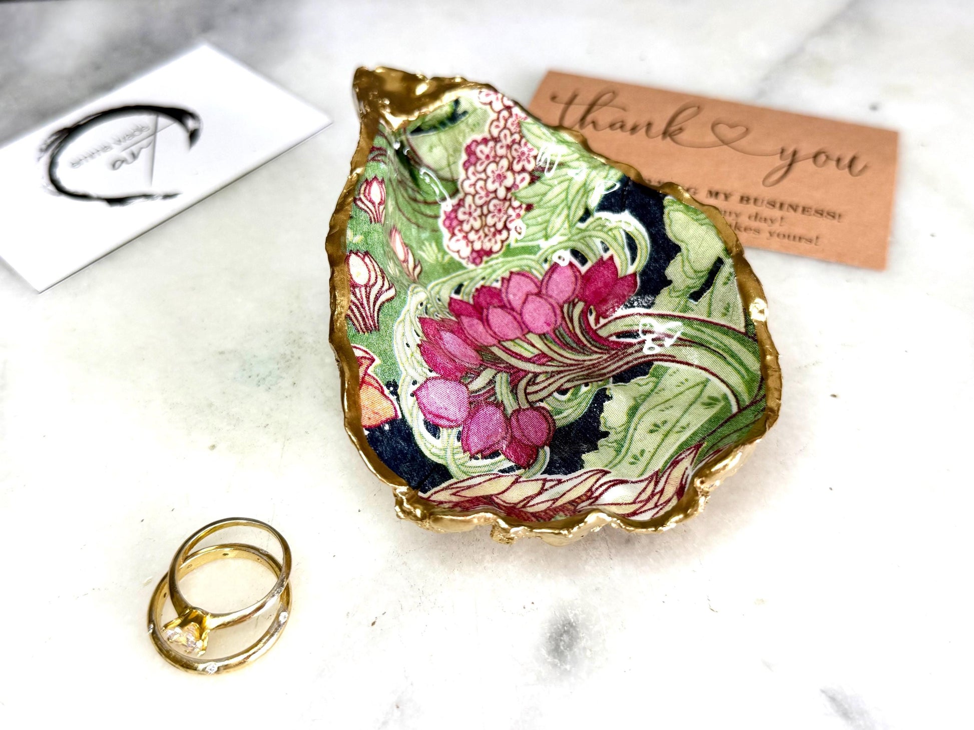Handcrafted V&A Museum Swirling Trees shell dish collection featuring large and small scallop shells and oyster shells decorated with flowing botanical artwork, pink water lilies and rich green foliage. Each natural Dorset shell is hand-gilded with real liquid gold leaf and sealed with crystal-clear resin. Luxury coastal decor, jewellery dishes, ring holders and trinket trays. Available individually or as a coordinated set of four shells.