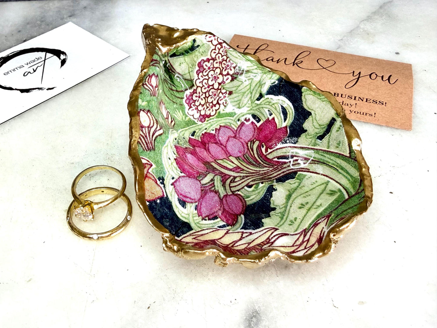 Handcrafted V&A Museum Swirling Trees shell dish collection featuring large and small scallop shells and oyster shells decorated with flowing botanical artwork, pink water lilies and rich green foliage. Each natural Dorset shell is hand-gilded with real liquid gold leaf and sealed with crystal-clear resin. Luxury coastal decor, jewellery dishes, ring holders and trinket trays. Available individually or as a coordinated set of four shells.