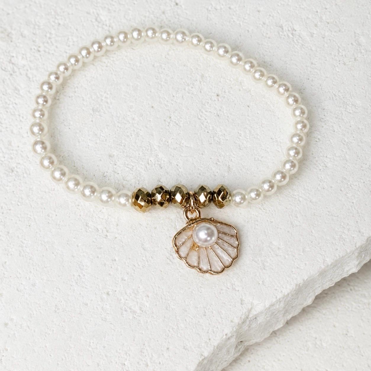 Set of three delicate coastal stretch bracelets featuring small ivory faux pearls and gold-tone seaside details. The coordinating jewellery set includes a blush enamel-style scallop shell charm with pearl centre, a textured gold starfish charm and a ridged gold shell centrepiece with pale champagne faceted beads. Lightweight 16 cm elasticated bohemian costume jewellery for coastal gifts, Christmas presents, stocking fillers, holidays, beach weddings, bridesmaids and gifts for her.