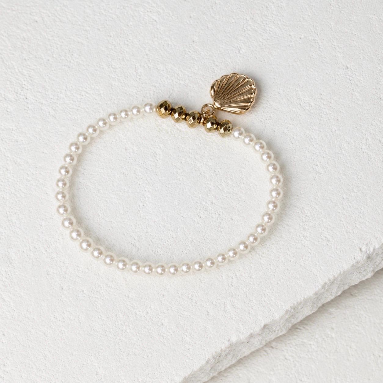 Set of three delicate coastal stretch bracelets featuring small ivory faux pearls and gold-tone seaside details. The coordinating jewellery set includes a blush enamel-style scallop shell charm with pearl centre, a textured gold starfish charm and a ridged gold shell centrepiece with pale champagne faceted beads. Lightweight 16 cm elasticated bohemian costume jewellery for coastal gifts, Christmas presents, stocking fillers, holidays, beach weddings, bridesmaids and gifts for her.