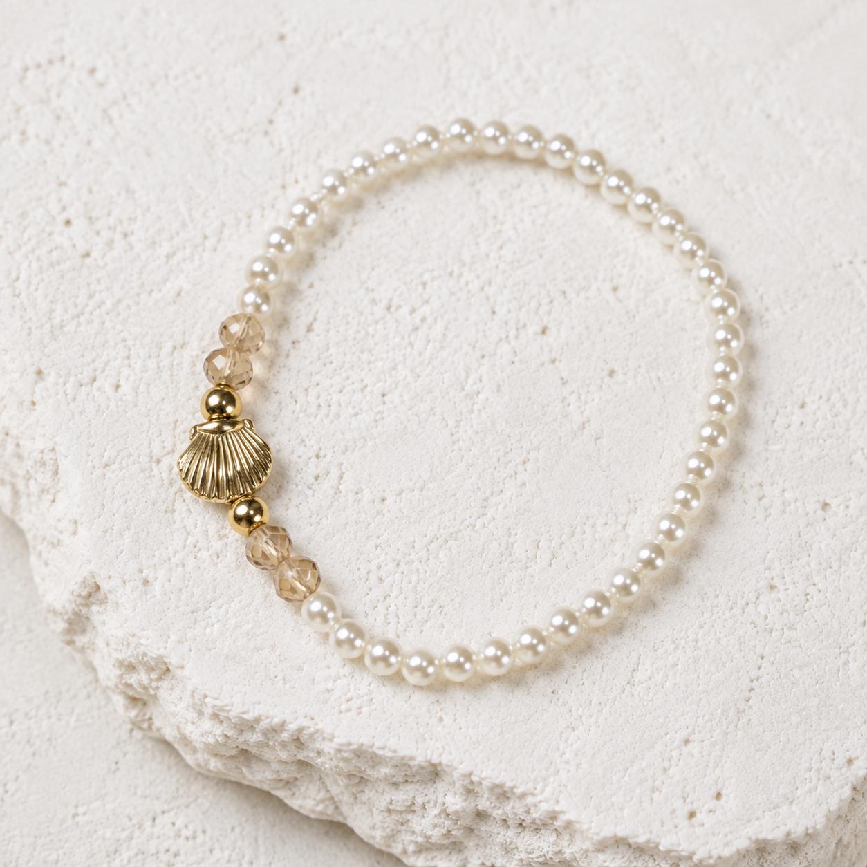 Set of three delicate coastal stretch bracelets featuring small ivory faux pearls and gold-tone seaside details. The coordinating jewellery set includes a blush enamel-style scallop shell charm with pearl centre, a textured gold starfish charm and a ridged gold shell centrepiece with pale champagne faceted beads. Lightweight 16 cm elasticated bohemian costume jewellery for coastal gifts, Christmas presents, stocking fillers, holidays, beach weddings, bridesmaids and gifts for her.