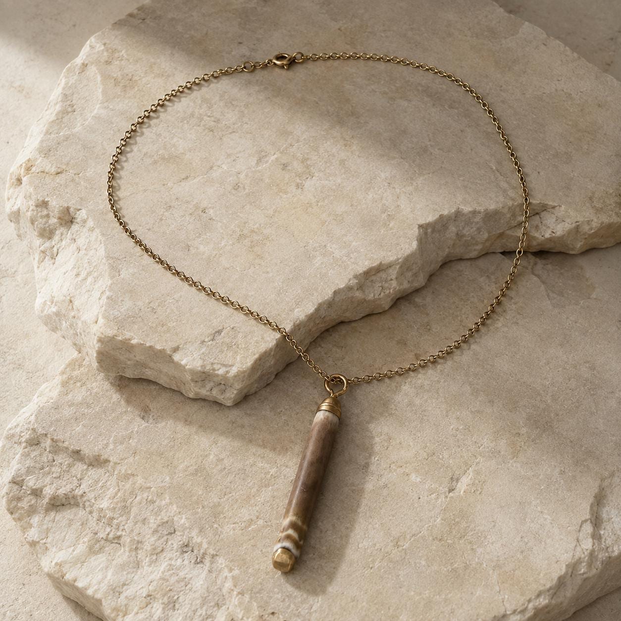 Close-up of a naturally banded sea-urchin spine pendant on beige travertine, showing its organic surface, gold-leaf tips and small attachment rin