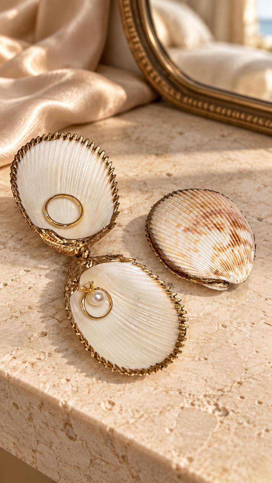 Handmade hinged cockle shell ring box with a natural white ridged interior and hand-finished gold-leaf edging. Available with a natural or gold-leaf outer shell, a natural or gold-speckled interior, and with no pearl or one pearl ring stop. A coastal jewellery box for storing rings and small treasured pieces.