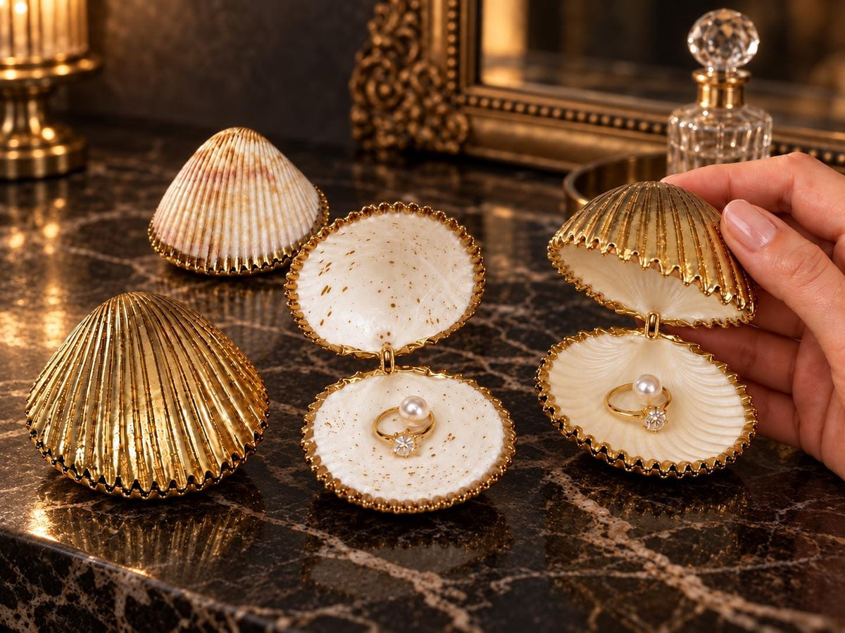 Handmade hinged cockle shell ring box with a natural white ridged interior and hand-finished gold-leaf edging. Available with a natural or gold-leaf outer shell, a natural or gold-speckled interior, and with no pearl or one pearl ring stop. A coastal jewellery box for storing rings and small treasured pieces. Very large cockle shells 12-13cm wide and can hold larger pieces of jewellery as well as rings and watches etc.